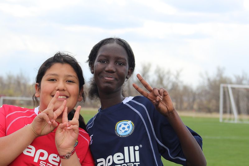 Two young Soccer Without Borders players flashing peace signs on the field